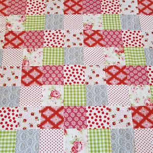 Könnte beinhalten: Eine Patchwork-Decke mit verschiedenen roten, weißen, grünen und grauen Blumenmustern. Die Decke besteht aus Quadraten aus verschiedenen Stoffen, jedes mit einem einzigartigen Design.