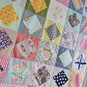 May include: A patchwork quilt with a diamond pattern. The quilt is made of various fabrics with floral, geometric, and polka dot patterns in shades of pink, blue, green, yellow, and red.