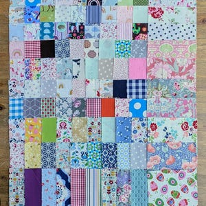 Könnte beinhalten: Eine rechteckige Patchwork-Deckenoberseite, bestehend aus zahlreichen kleinen Stoffrechtecken und -quadraten in verschiedenen Farben und Mustern, darunter Blumen-, geometrische, gestreifte und Tiermotive, angeordnet in einem gitterartigen Layout mit sichtbaren Nähten.