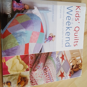 Könnte beinhalten: Buchcover mit dem Titel "Kids' Quilts in a Weekend" und einem farbenfrohen Patchwork-Quilt-Design. Das Buch enthält 20 Projekte, die für Babys bis zu 10-Jährigen geeignet sind.