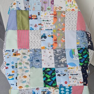 May include: A patchwork quilt made of various colorful fabrics featuring different patterns and designs. The quilt is made up of squares with different themes, including animals, vehicles, and dinosaurs. The quilt is displayed on a wooden chair.
