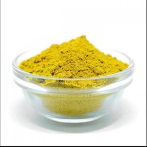 Puede incluir: Un pequeño bol de vidrio lleno de un polvo amarillo brillante. El polvo es probablemente una especia o condimento.