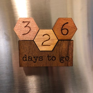 May include: Wooden countdown calendar with hexagonal tiles showing the numbers 3, 2, and 6. The tiles are arranged in a honeycomb pattern and are mounted on a rectangular wooden base. The base has the text "days to go" engraved on it.