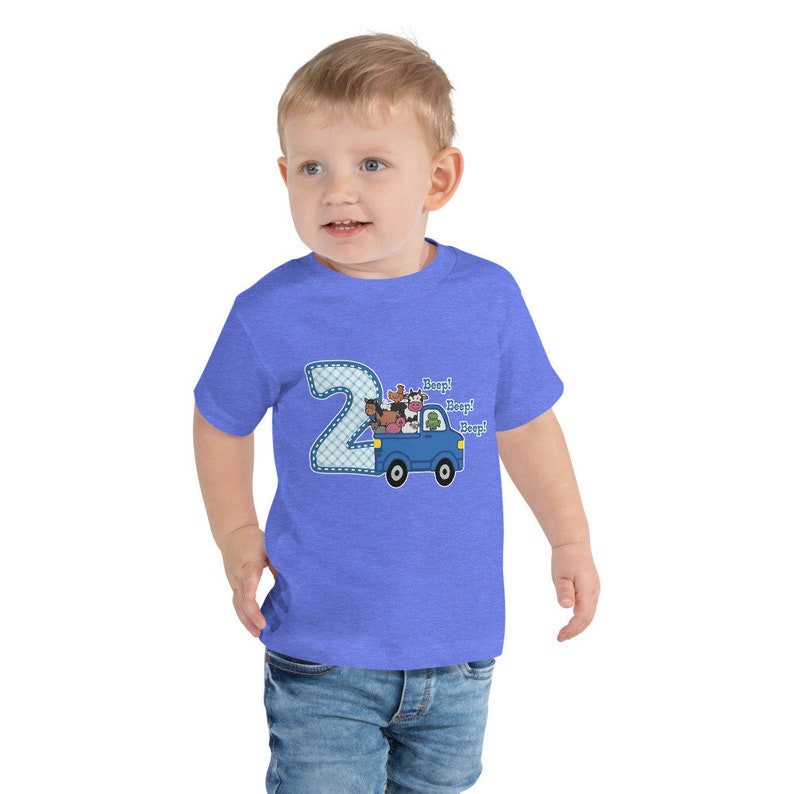 May include: A toddler wearing a blue t-shirt with a blue and white number 2 on the front. The number 2 has a blue truck with farm animals inside. The text "Beep! Beep! Beep!" is above the truck.