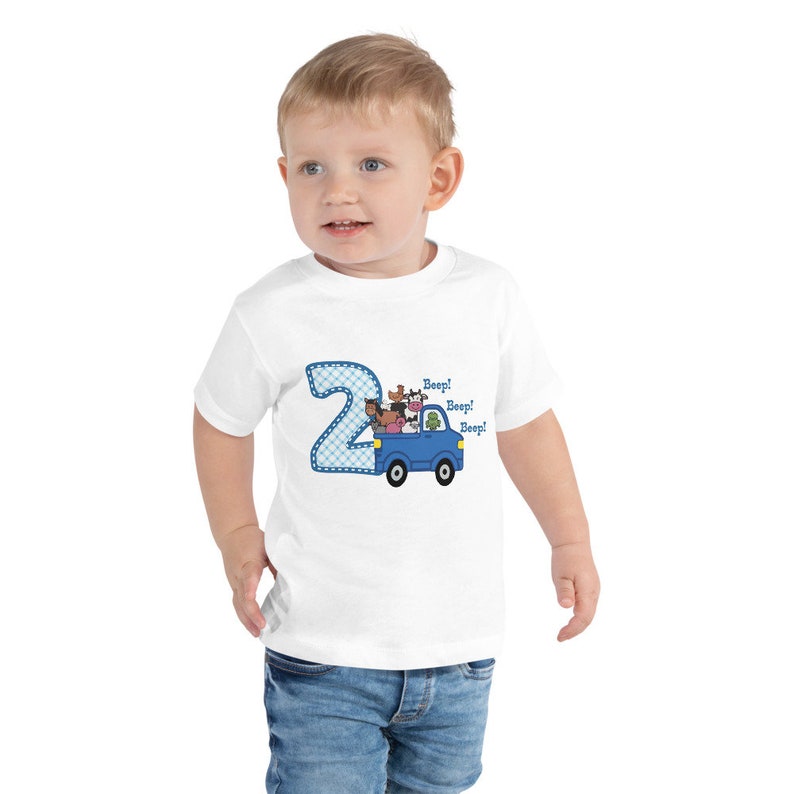 May include: White short-sleeved t-shirt with a blue number 2 and a blue truck with farm animals. The text "Beep! Beep! Beep!" is on the shirt.