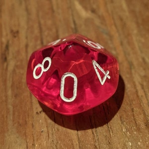 May include: A red, clear, faceted, 10-sided die with white numbers. The die is showing the number 0.