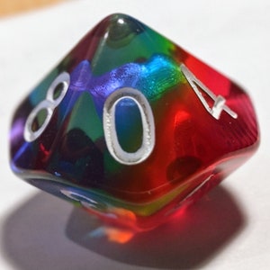 Pode incluir: Um dado transparente e iridescente multicolorido com números brancos. O dado mostra o número 4.