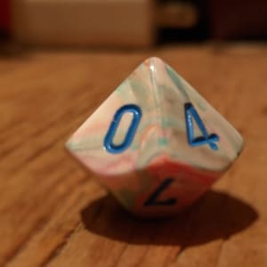 以下が含まれることがあります： 青色の数字が書かれた白、ピンク、緑の6面ダイス。ダイスは4を示しています。