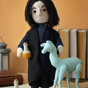 May include: Crocheted doll of a fictional character with long black hair, wearing a black coat and blue shirt, holding a yellow potion bottle. A blue crocheted animal stands next to the doll.