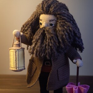 Pode incluir: Um brinquedo de pel&uacute;cia de croch&ecirc; de um mago com uma longa barba e cabelo castanho, vestindo um casaco marrom e segurando uma lanterna e um guarda-chuva rosa.