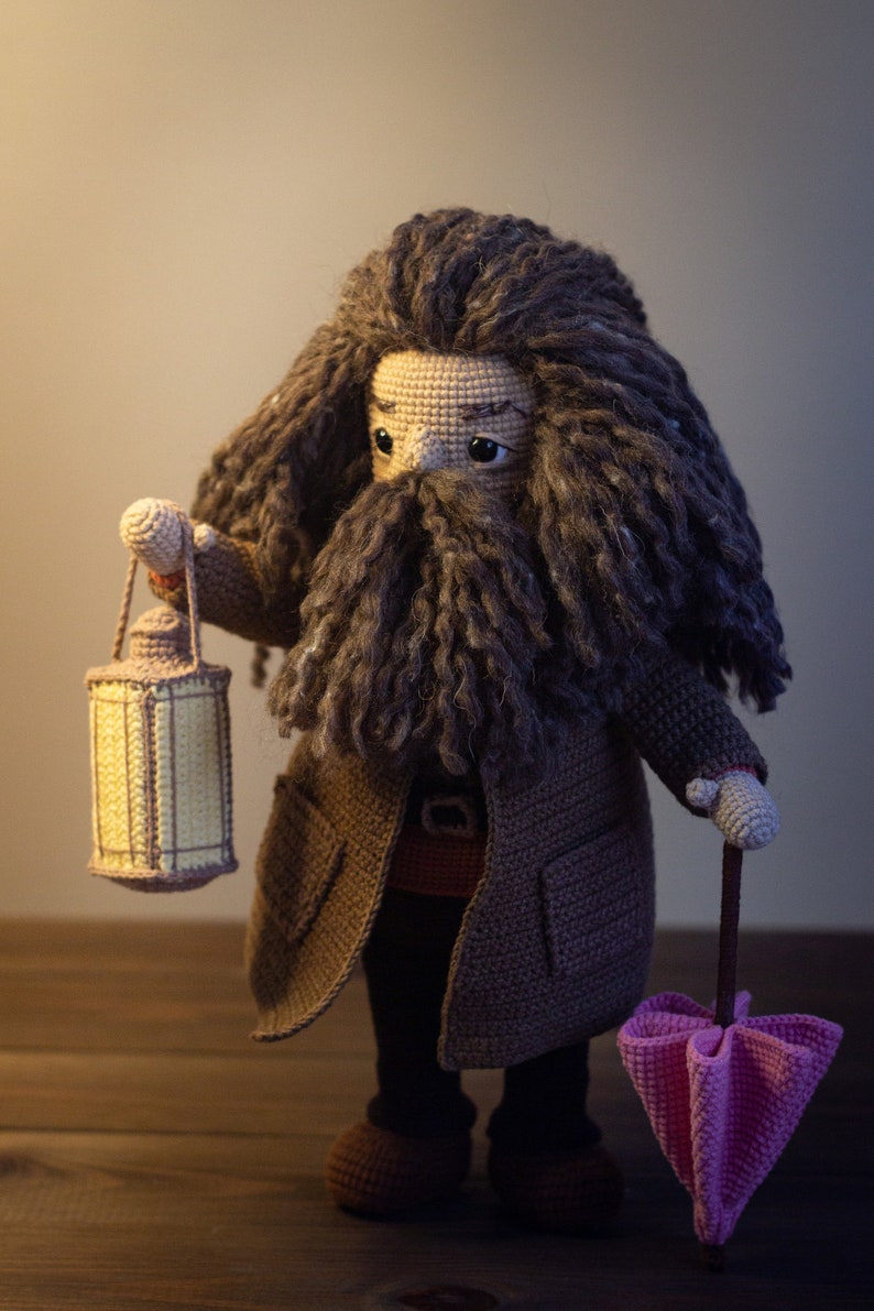 Pode incluir: Um brinquedo de pel&uacute;cia de croch&ecirc; de um mago com uma longa barba e cabelo castanho, vestindo um casaco marrom e segurando uma lanterna e um guarda-chuva rosa.