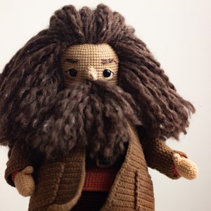 Pode incluir: Boneca de croch&ecirc; com cabelo castanho e barba, vestindo um casaco marrom e uma camisa vermelha.