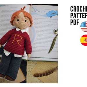May include: Crochet pattern PDF for a red and brown amigurumi doll with a white shirt and a letter "R" on the sweater. The doll is sitting on a book with a feather and a blue car illustration.