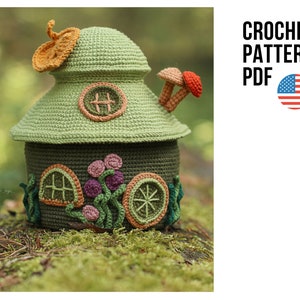 Puede incluir: Patrón de crochet PDF para una casa amigurumi verde y marrón con un techo de hongo y una puerta. La casa tiene una ventana y flores en el lateral.