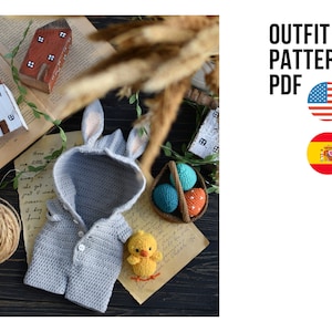 以下が含まれることがあります： 赤ちゃん用の編みぐるみウサギの衣装。グレーのフード付きジャケットとウサギの耳が付いています。衣装は、カラフルな編みぐるみイースターエッグの入ったバスケットと一緒に木製の表面に置かれています。