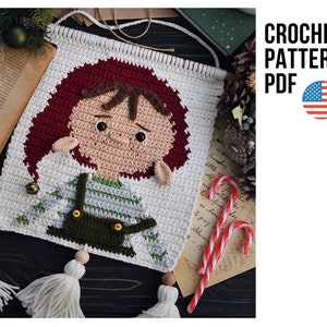 May include: Crochet pattern PDF for a Christmas elf wall hanging. The elf is wearing a red hat, a green and white striped shirt, and brown overalls. The pattern is available for download in the United States.
