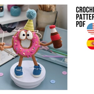 Puede incluir: Un personaje de donut de ganchillo con un gorro de fiesta, bigote y una botella de refresco. El donut es rosa con chispas, brazos y piernas marrones y zapatos azules. La imagen incluye el texto "CROCHET PATTERN PDF".