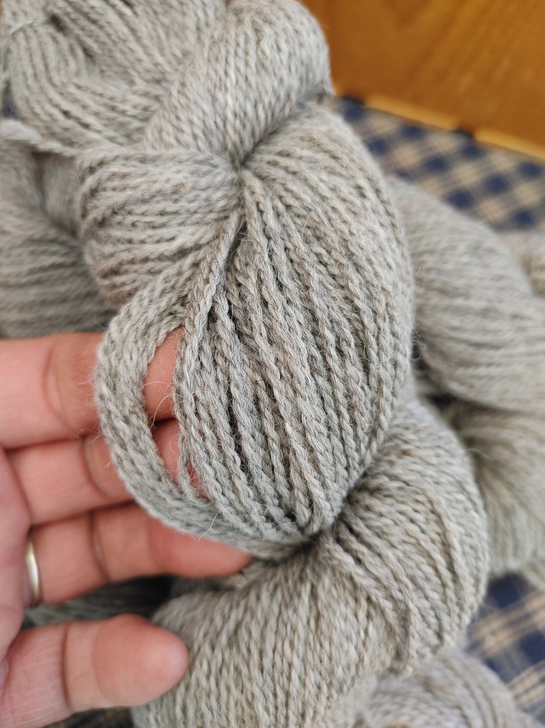 May include: A skein of light gray yarn, made of wool, with a soft, fuzzy texture.