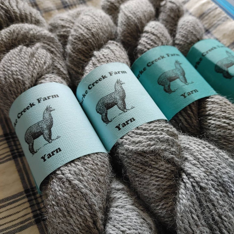 May include: Four skeins of gray alpaca yarn with blue labels that say "Alpac Creek Farm Yarn" and feature a black and white illustration of an alpaca.