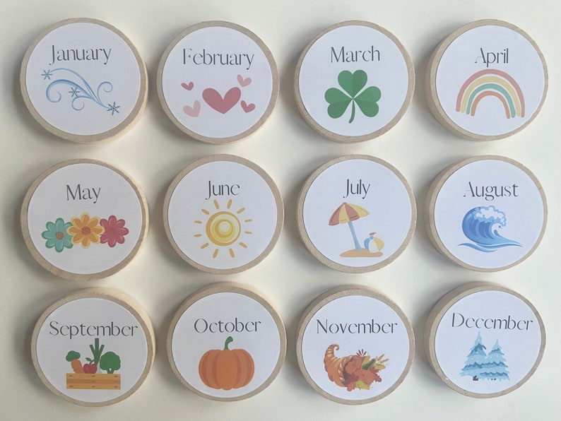 May include: Twelve wooden circles with a white background and black text, each representing a month of the year. Each circle has a small illustration representing the month, such as snowflakes for January, hearts for February, a shamrock for March, a rainbow for April, flowers for May, a sun for June, an umbrella for July, a wave for August, vegetables for September, a pumpkin for October, a cornucopia for November, and a pine tree for December.