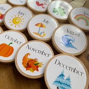 May include: Twelve wooden circles with the months of the year printed on them. Each circle has a different image representing the month. For example, January has a snowflake, February has a heart, March has a shamrock, April has a rainbow, May has a flower, June has a sun, July has an umbrella and beach ball, August has a wave, September has a pumpkin, October has a cornucopia, November has a turkey, and December has a pine tree.