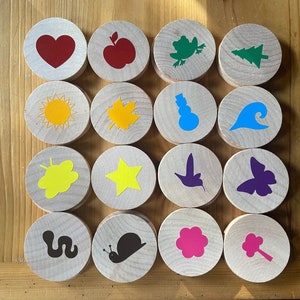 May include: Set of 16 wooden circles with various colorful images, including a heart, apple, tree, sun, leaf, snowman, wave, butterfly, star, hummingbird, flower, and snail.