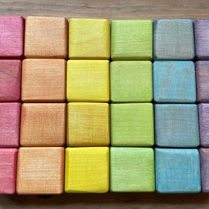 Puede incluir: Un conjunto de 20 bloques de madera en un degradado de colores arcoíris. Los bloques están dispuestos en cuatro filas de cinco bloques cada una. Los bloques son todos del mismo tamaño y forma, y están hechos de madera natural lisa.