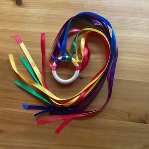 May include: A rainbow ribbon wand with a white wooden ring in the center. The ribbons are tied together at the ring and are red, orange, yellow, green, blue, and purple.