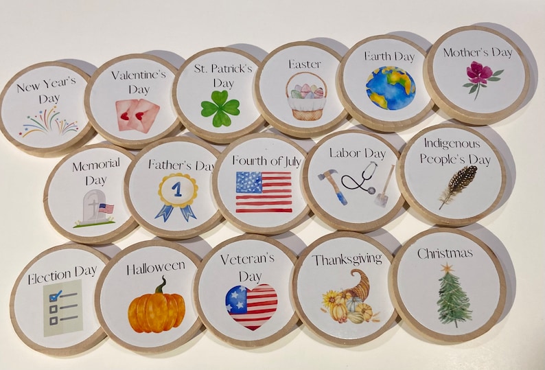May include: A set of 16 round wooden tokens with illustrations and text representing different holidays throughout the year.  The tokens feature images such as fireworks, hearts, shamrocks, Easter eggs, a globe, a flower, a tombstone, a number one, an American flag, a hammer, a stethoscope, a feather, a pumpkin, a heart with stars, a cornucopia, and a Christmas tree.