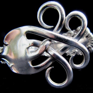 May include: A silver bracelet made from a repurposed fork, with the tines twisted into a decorative design.