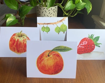 May include: Four watercolour greeting cards featuring different fruits. The cards are white with a red apple, a peach, a strawberry, and a branch of green gooseberries.