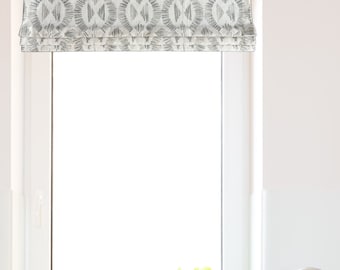 May include: A white window with a gray patterned roman shade. There are three potted plants on the window sill, two gray pots and one white pot. A black sink with a chrome faucet is below the window.