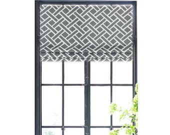May include: A gray and white geometric patterned roman shade is mounted on a window with black trim. The window is in a room with white cabinets and a white countertop.
