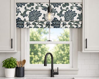 May include: A Roman blind featuring a white fabric base with a dark blue and green floral pattern, installed over a kitchen window. The blind is positioned above a black tap, a sink, and light grey cabinets with black hardware.