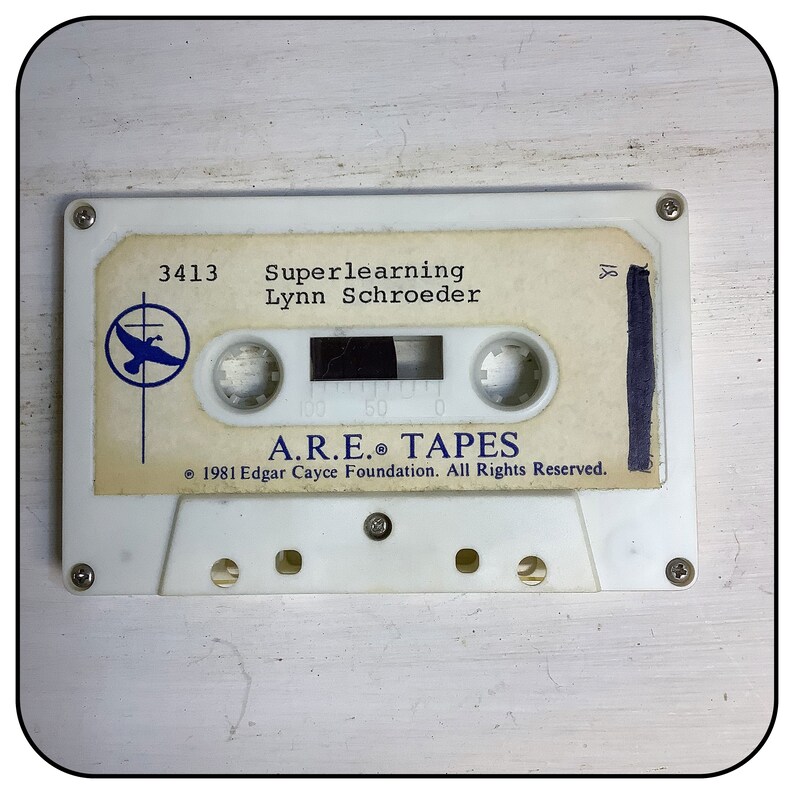 May include: A white cassette tape featuring a label with the text 3413 Superlearning Lynn Schroeder, a blue bird logo, and A.R.E. TAPES 1981 Edgar Cayce Foundation. The cassette has four visible screws and a central window showing dark magnetic tape.