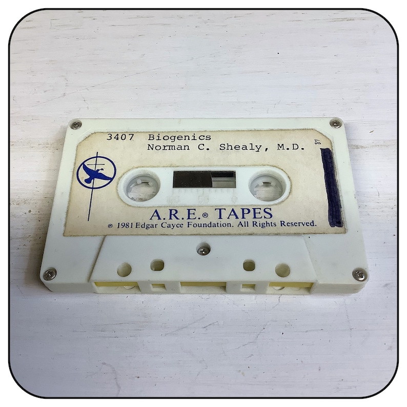 Może przedstawiać: Biała kaseta magnetofonowa z etykietą zawierającą tekst 3407 Biogenics Norman C. Shealy, M.D. oraz A.R.E. TAPES 1981 Edgar Cayce Foundation. All Rights Reserved. Po lewej stronie nadrukowano niebieskie okrągłe logo z sylwetką ptaka.