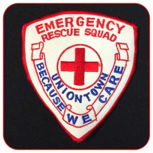 May include: White embroidered patch with red trim. The patch features a red cross, the words "Emergency Rescue Squad", and the text "Because We Care Uniontown" in a blue banner.