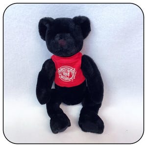 May include: Black plush teddy bear wearing a red shirt with a white logo that says "Service Quality Excellence".