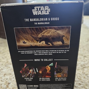 Puede incluir: Una caja negra de figuras de acci&oacute;n de Star Wars con "The Mandalorian & Grogu". La caja incluye una imagen de una bestia Mudhorn y texto que describe la escena. Im&aacute;genes adicionales muestran otros personajes para coleccionar.