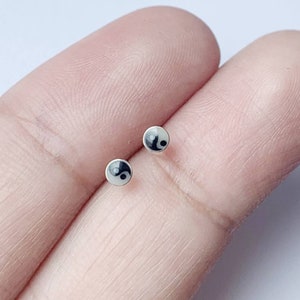 May include: A pair of silver stud earrings with a black and white yin yang symbol on each earring.