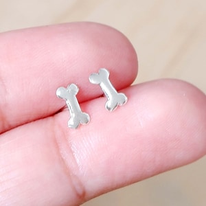 May include: A pair of silver bone-shaped stud earrings. The earrings are small and delicate, and they would make a great gift for a dog lover.