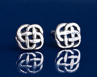 May include: A pair of silver-toned stud earrings featuring a circular, interwoven knot design. The metal has a textured, metallic finish with visible loops and gaps forming a symmetrical pattern. The earrings are displayed as a pair of studs.