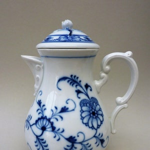 Könnte beinhalten: Eine weiße Porzellan-Kaffeekanne mit blau-weißem Blumenmuster. Die Kanne hat einen Deckel und einen Henkel.