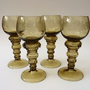 Op de afbeelding: Set van vier wijnglazen van amberkleurig glas met gegraveerde bloemmotieven en een unieke, bolle steel.