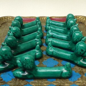 May include: A set of 10 green ceramic dachshund dog shaped  chopstick rests. The rests are arranged in a row on a gold and red tray.
