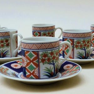 以下が含まれることがあります： 6客のセラミックティーカップとソーサーのセット。各カップとソーサーは、赤、青、緑の木、花、幾何学模様の詳細なデザインが施された白いベースが特徴です。カップには取っ手があり、高さは約7.6cmです。