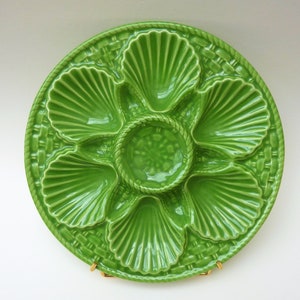Peut inclure: Une assiette à huîtres en céramique verte avec six compartiments individuels en forme de coquille et un puits central. L'assiette a un motif de panier tissé.