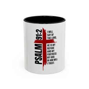 May include: A white ceramic mug with a black interior and rim. The exterior features a red cross graphic behind black text that reads: PSALM 91:2 I WILL SAY OF THE LORD, HE IS MY REFUGE AND MY FORTRESS: MY GOD; IN HIM WILL I TRUST.