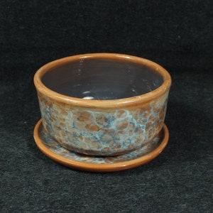 Può includere: Un vaso di terracotta marrone con una smaltatura marmorea blu e bianca. Il vaso ha un sottovaso.