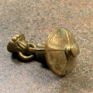 Peut inclure: Un bouton de tiroir en laiton vintage avec un design orné. La poignée présente une poignée décorative et une plaque arrière arrondie. Le laiton a un aspect vieilli, avec des reflets verts. Le design général suggère un style classique ou antique.